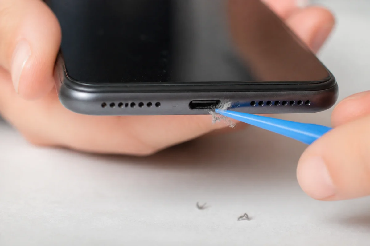 Nettoyage délicat du port de charge d’un smartphone avec un outil plastique pour retirer poussières et fibres